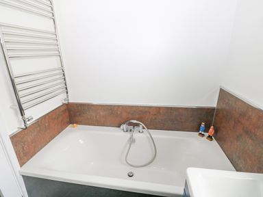 A bathtub with a handheld showerhead and two small figurines on the edge at Hillbrook House in Nolton Haven
