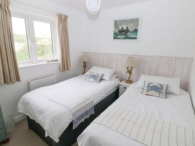 A bedroom with two single beds nightstands with lamps a window and a painting above the beds at Hillbrook House in Nolton Haven