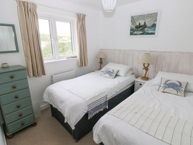 A bedroom with two single beds separated by a nightstand with lamps a chest of drawers and a window with curtains at Hillbrook House in Nolton Haven