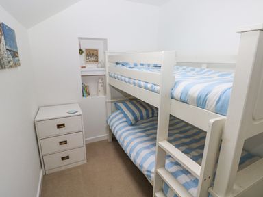 A small bedroom with a white bunk bed striped blue and white bedding and a white three drawer chest at Hillbrook House in Nolton Haven