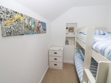 A small bedroom with white bunk beds striped blue and white bedding a white chest of drawers and wall art above the chest at Hillbrook House in Nolton Haven