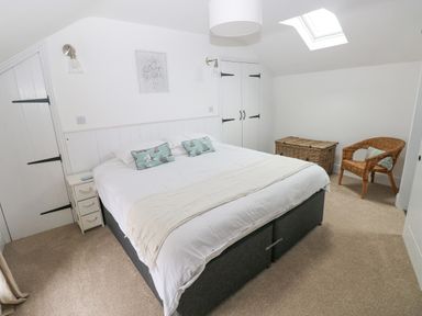 A bedroom with a large bed two bedside tables wicker chair and wicker storage chest at Hillbrook House in Nolton Haven
