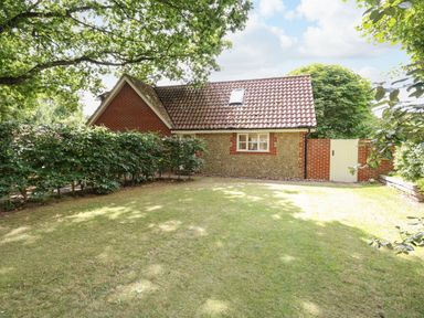 A garden with a lawn and a small house with a tiled roof and brick and stone walls at Oak Tree Lodge in Crostwick near Norwich
