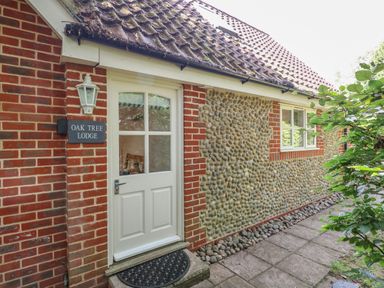 An exterior view of a brick and stone cottage with a white door and window at Oak Tree Lodge in Crostwick near Norwich