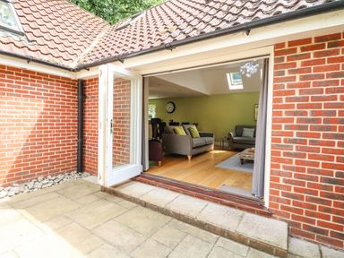 An open door leading from a brick patio to a living room with sofas and wooden floor at Oak Tree Lodge in Crostwick near Norwich