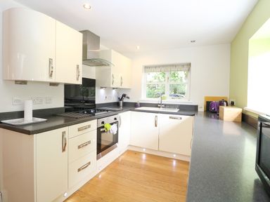A kitchen with white cabinets black countertops an oven a stovetop a sink under a window and various small appliances at Oak Tree Lodge in Crostwick near Norwich