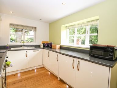 A kitchen with white cabinets black countertops a microwave toaster kettle and two windows at Oak Tree Lodge Crostwick near Norwich