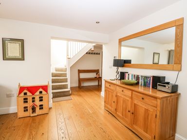 A hallway with wooden floor a staircase a wooden cabinet with books and a lamp and a wooden dollhouse at Oak Tree Lodge Crostwick near Norwich