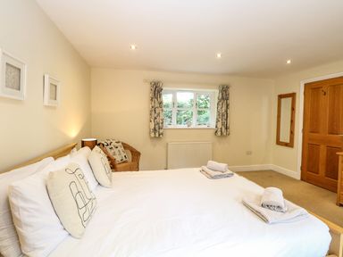 A bedroom with a bed with pillows and folded towels a wicker chair near a window and a wooden door at Oak Tree Lodge in Crostwick near Norwich