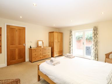 A bedroom with a double bed towels on bed wooden dresser wardrobe and glass doors with curtains at Oak Tree Lodge in Crostwick near Norwich