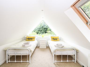 A bedroom with two single beds and a white nightstand under a triangular window at Oak Tree Lodge in Crostwick near Norwich