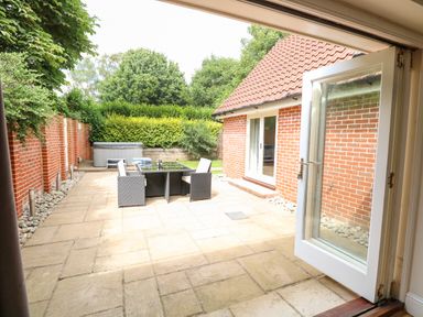 A patio with a glass table and four chairs next to a brick building with an open glass door at Oak Tree Lodge Crostwick near Norwich