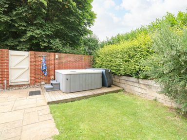 An outdoor space with a hot tub on a wooden platform and a brick wall with a white gate at Oak Tree Lodge in Crostwick near Norwich