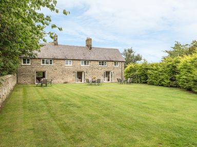A stone house with multiple patio doors opening to a grassy lawn with outdoor tables and chairs at Dorothy's Cottage in Alnmouth