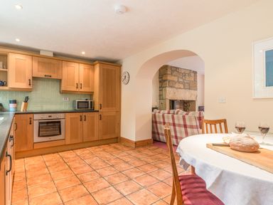A kitchen with wooden cabinets a tiled floor and a round dining table with bread and wine at Dorothy's Cottage in Alnmouth