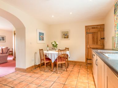 A dining area with a round table set with a white tablecloth and four wooden chairs in a kitchen at Dorothys Cottage in Alnmouth