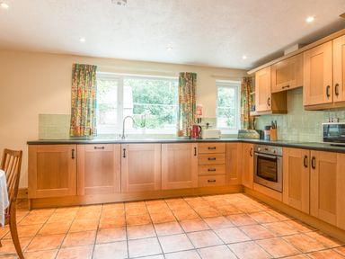 A kitchen with wooden cabinets tiled floor and windows with patterned curtains at Dorothy's Cottage in Alnmouth