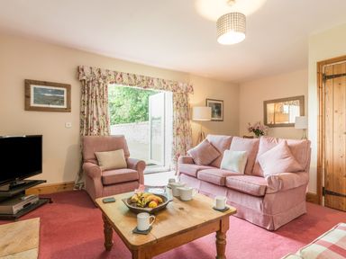 A living room with pink armchairs a wooden coffee table with tea set and fruit bowl and a television at Dorothy's Cottage in Alnmouth