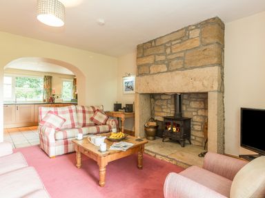A living room with a stone fireplace wooden coffee table checkered sofa and an open archway to the kitchen at Dorothys Cottage in Alnmouth