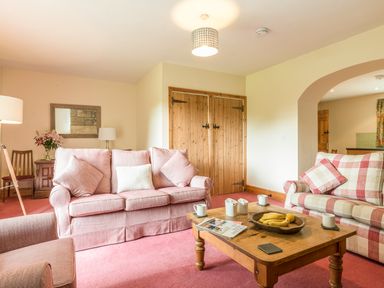A living room with two sofas a wooden coffee table with fruit and cups and a wooden cabinet at Dorothy's Cottage in Alnmouth