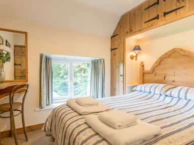 A bedroom with a striped bedspread a wooden chair and desk a window with curtains and wooden cupboards at Dorothy's Cottage in Alnmouth