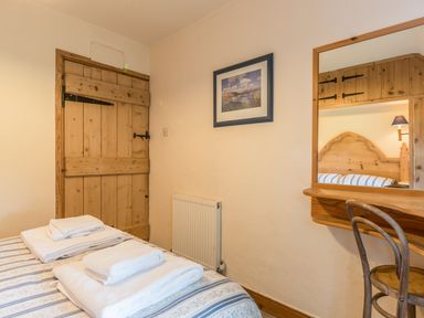 A bedroom with a wooden door folded towels on a bed and a wooden desk with mirror at Dorothy's Cottage in Alnmouth