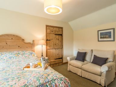 A bedroom with a floral bedspread a wooden door a lamp a beige sofa with cushions and a framed picture on the wall at Dorothy's Cottage in Alnmouth