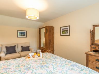 A bedroom with a floral bedspread a wooden wardrobe a beige sofa and a wooden dresser at Dorothy's Cottage in Alnmouth