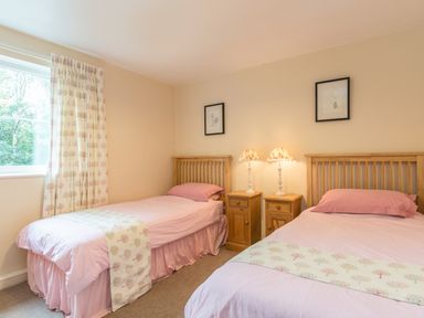 A bedroom with two single beds pink bedding wooden headboards two bedside tables with lamps and curtains at Dorothy's Cottage in Alnmouth