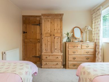 A bedroom with wooden door wardrobe and chest of drawers between two beds at Dorothys Cottage in Alnmouth