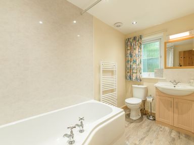 A bathroom with a bathtub toilet sink and a window with floral curtains at Dorothy's Cottage in Alnmouth