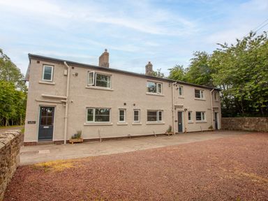 A two-story building with multiple windows and doors surrounded by trees at Dorothy's Cottage in Alnmouth