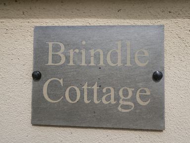 A gray stone plaque with the words Brindle Cottage fixed to a rough beige wall at Brindle Cottage Royal Wootton Bassett
