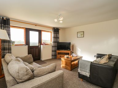 A living room with two sofas a wooden coffee table a television and a door with windows at Brindle Cottage in Royal Wootton Bassett