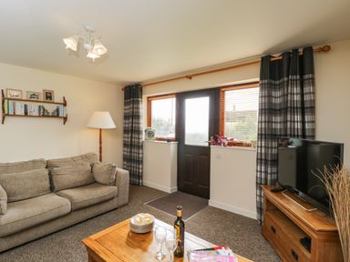 A living room with a sofa coffee table TV and door with windows at Brindle Cottage in Royal Wootton Bassett