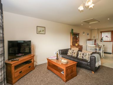A living room with a black leather sofa and wooden furniture at Brindle Cottage in Royal Wootton Bassett