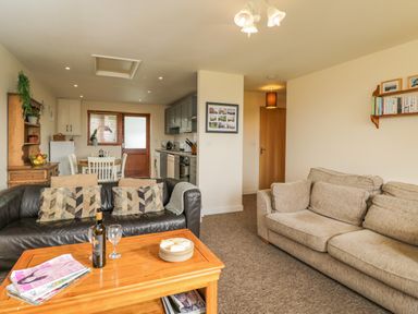 A living room with two sofas a wooden coffee table and an open kitchen at Brindle Cottage in Royal Wootton Bassett