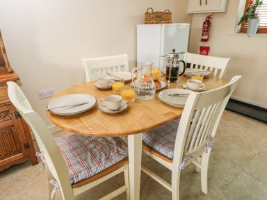 A dining table with four chairs set with plates cups glasses of orange juice a jug and a French press in a kitchen at Brindle Cottage in Royal Wootton Bassett