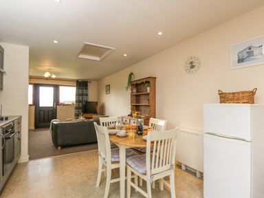 A kitchen and dining area with a wooden table and four chairs next to a white refrigerator and wooden cupboard in an open plan room at Brindle Cottage in Royal Wootton Bassett