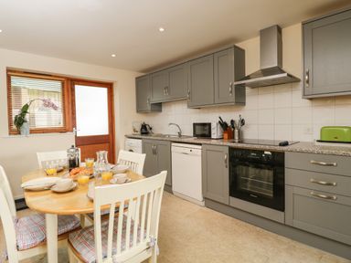 A kitchen with gray cabinets a wooden dining table set with breakfast dishes and a door with window blinds at Brindle Cottage in Royal Wootton Bassett
