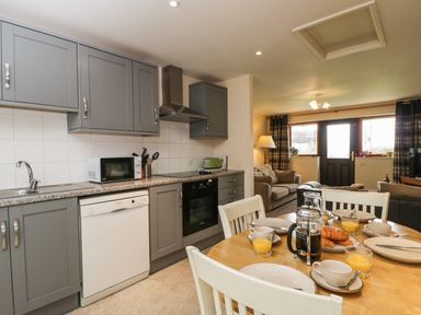 A kitchen with grey cabinets and appliances next to a dining table set with plates cups orange juice and croissants at Brindle Cottage in Royal Wootton Bassett