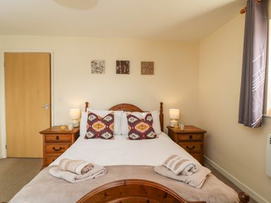 A bedroom with a wooden bed and bedside tables with lamps at Brindle Cottage in Royal Wootton Bassett