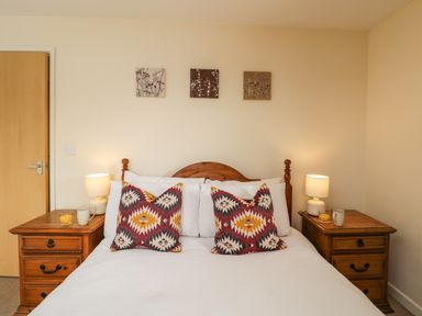 A bedroom with a double bed two patterned pillows two bedside tables lamps and cups at Brindle Cottage in Royal Wootton Bassett