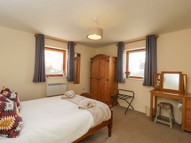 A bedroom with a double bed two windows wooden wardrobe dressing table and stool at Brindle Cottage in Royal Wootton Bassett