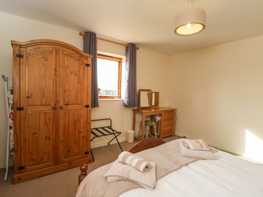 A bedroom with a wooden wardrobe a window with curtains a desk with a mirror and a bed with towels at Brindle Cottage in Royal Wootton Bassett