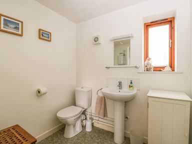 A bathroom with a toilet sink mirror small window cabinet and pictures on the wall at Brindle Cottage in Royal Wootton Bassett