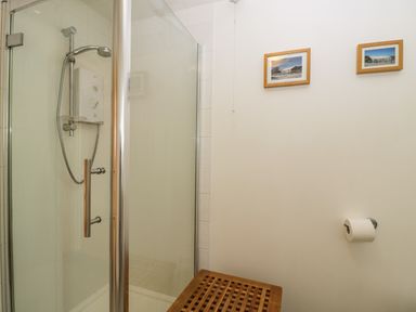 A bathroom with a glass shower enclosure a wooden bench two framed pictures on the wall and a toilet paper holder at Brindle Cottage in Royal Wootton Bassett