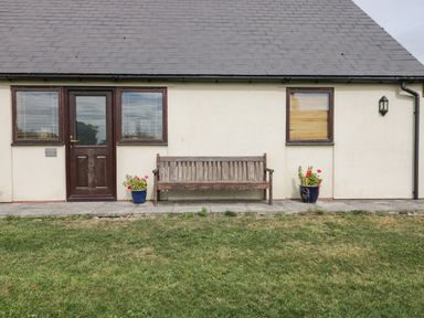 The front of a cottage with a wooden door two windows a wooden bench two flowerpots and a grassy lawn at Brindle Cottage in Royal Wootton Bassett