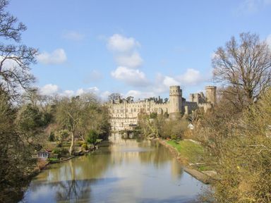 A river with trees on both sides and a large stone castle in the background at Highcroft in Stratford-Upon-Avon