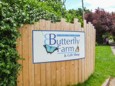 A wooden fence with a sign for Butterfly Farm and Gift Shop next to a grassy path with two people in Stratford-Upon-Avon